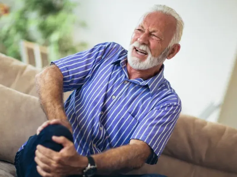Older man wincing in pain while holding his leg at home